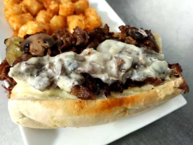Enjoy and hot and melty steak bomb at Cheers Grille & Bar in Concord NH, topped with mushrooms and melted cheese and served with Tater Tots.